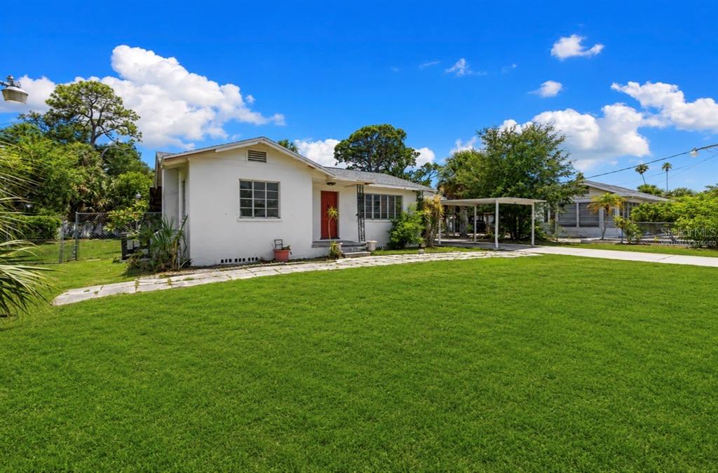A white single-story house with a red front door and a carport on a lawn — 2025 17TH AVENUE W, BRADENTON, FL