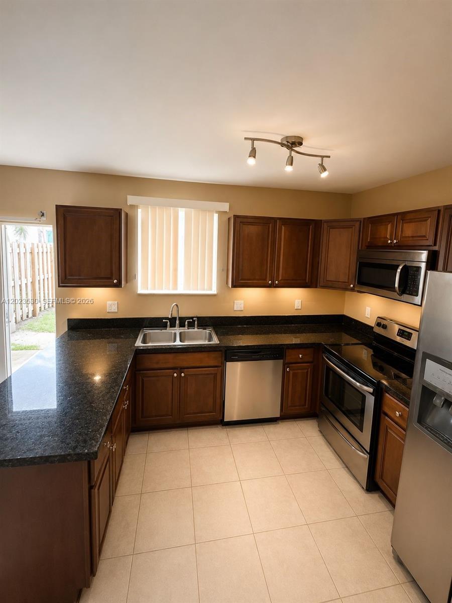 A kitchen features dark wood cabinets, black granite countertops, stainless steel appliances, and tile flooring — 1827 NW 142nd Ln, Opa-Locka FL 33054, OPA-LOCKA, FL