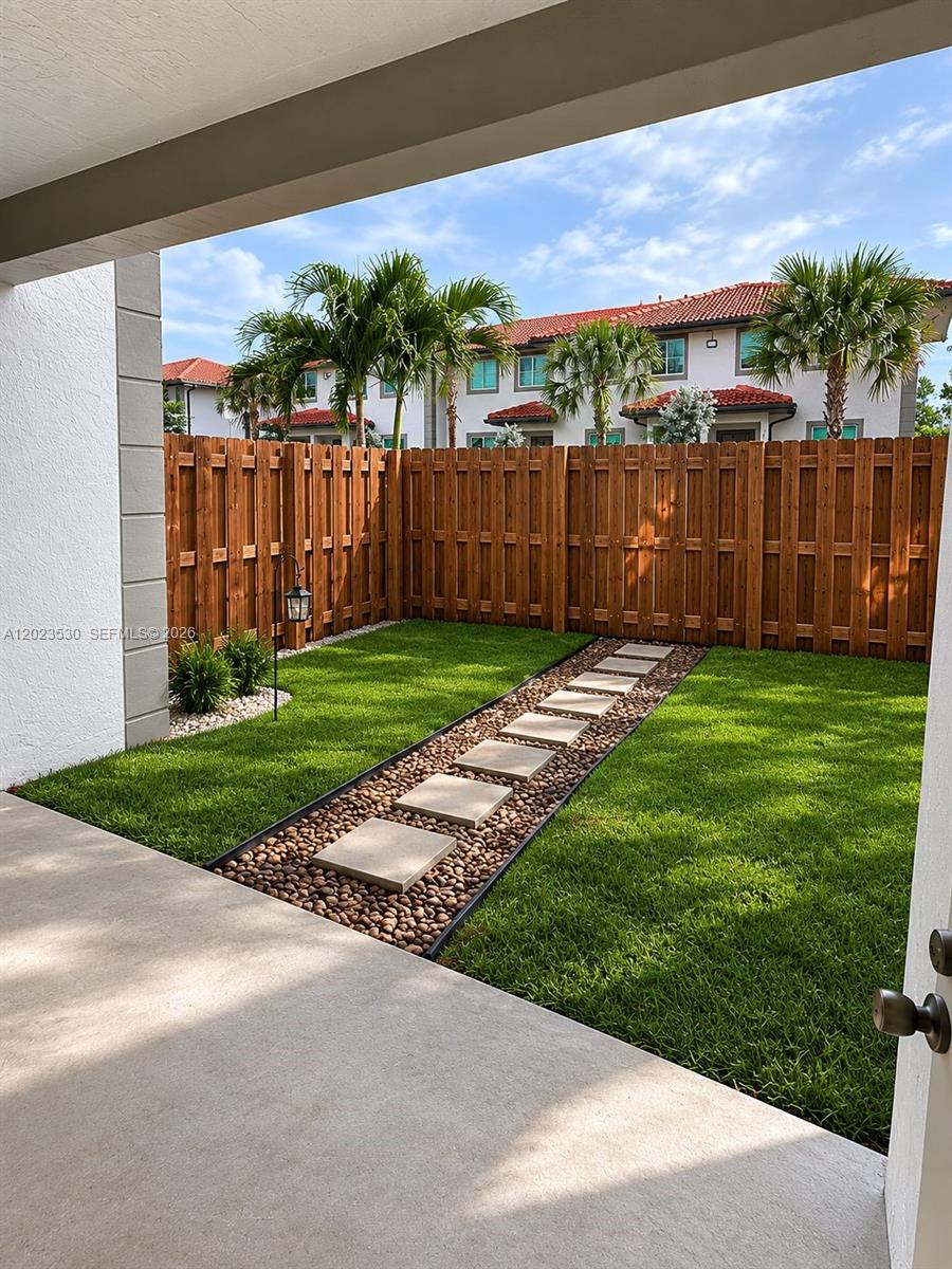 A small backyard features a stone paver path, green grass, and a wooden privacy fence — 1827 NW 142nd Ln, Opa-Locka FL 33054, OPA-LOCKA, FL