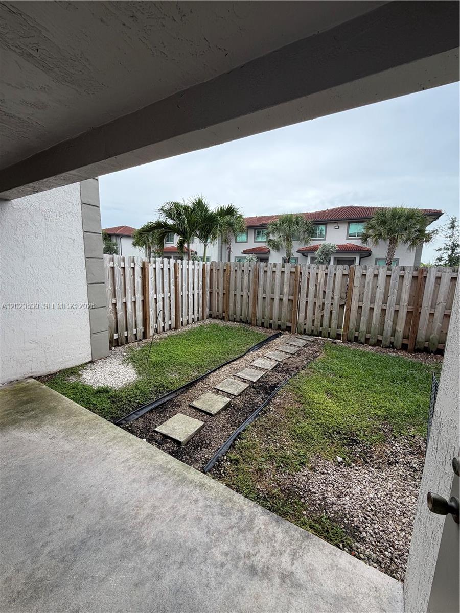 A small fenced backyard features a concrete patio, a grass lawn, and a stone path — 1827 NW 142nd Ln, Opa-Locka FL 33054, OPA-LOCKA, FL