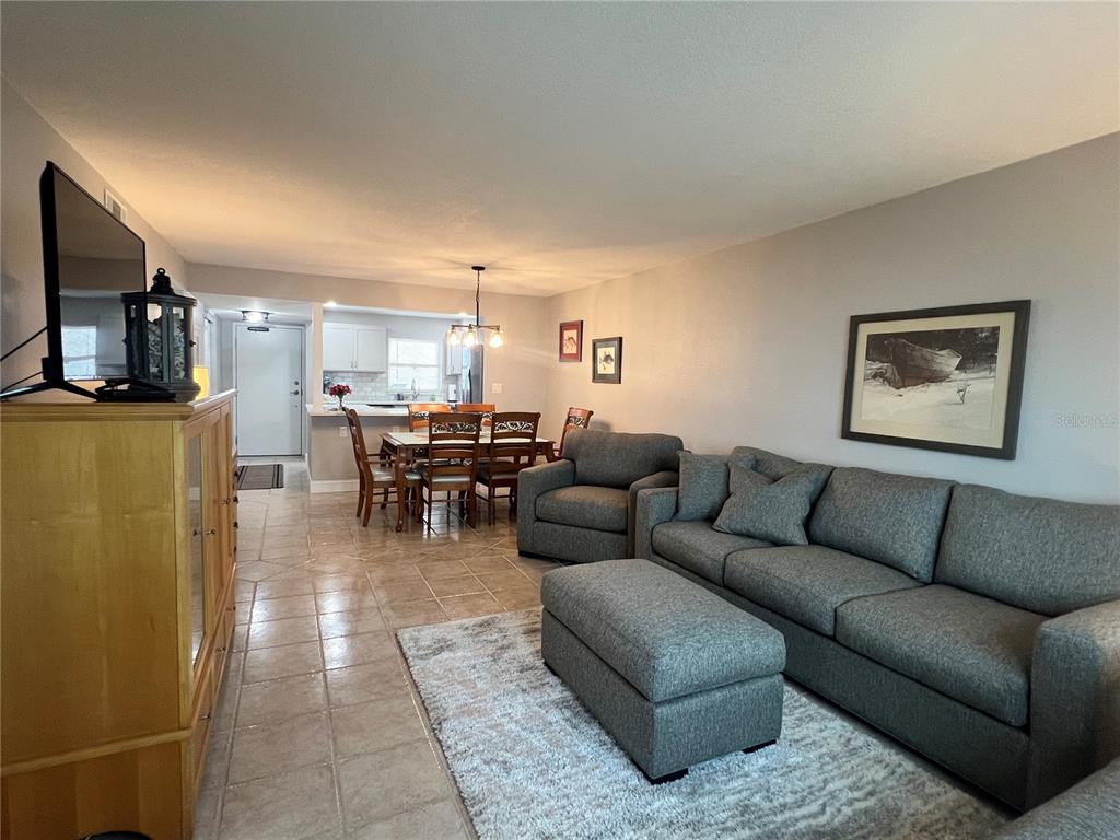 A living room with gray furniture and tile flooring opens to a dining area and kitchen — 1270 GULF BOULEVARD UNIT 1403, CLEARWATER, FL