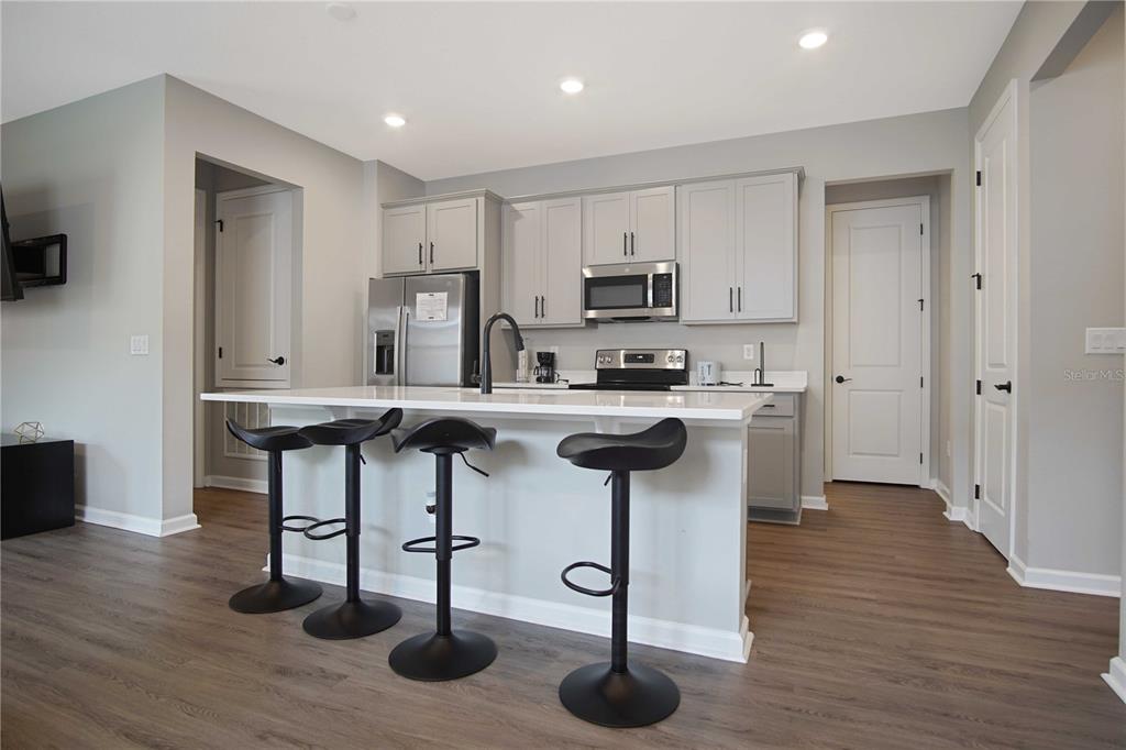 A kitchen with a white island, black bar stools, grey cabinets, and wood-look flooring — 832 BLUE CREEK DRIVE, HAINES CITY, FL