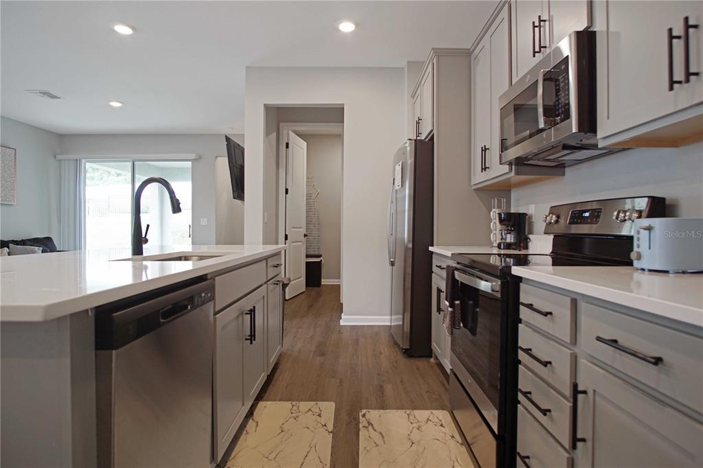 A modern kitchen features gray cabinets, stainless steel appliances, and a white quartz island — 832 BLUE CREEK DRIVE, HAINES CITY, FL