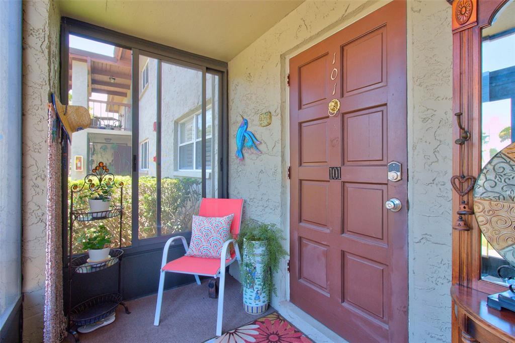 A covered entryway features a brown door, a pink chair, and a metal plant stand — 1001 S BAYSHORE BOULEVARD UNIT 101, SAFETY HARBOR, FL