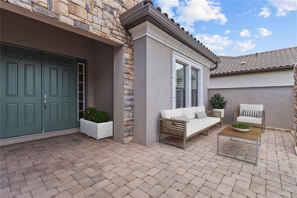 A paved courtyard features a double door entrance, stone accents, and outdoor patio furniture — 9913 WICKER PARK PLACE, PALMETTO, FL