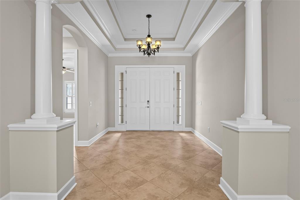 A foyer features a tray ceiling, a chandelier, tile flooring, and two white decorative columns — 9913 WICKER PARK PLACE, PALMETTO, FL