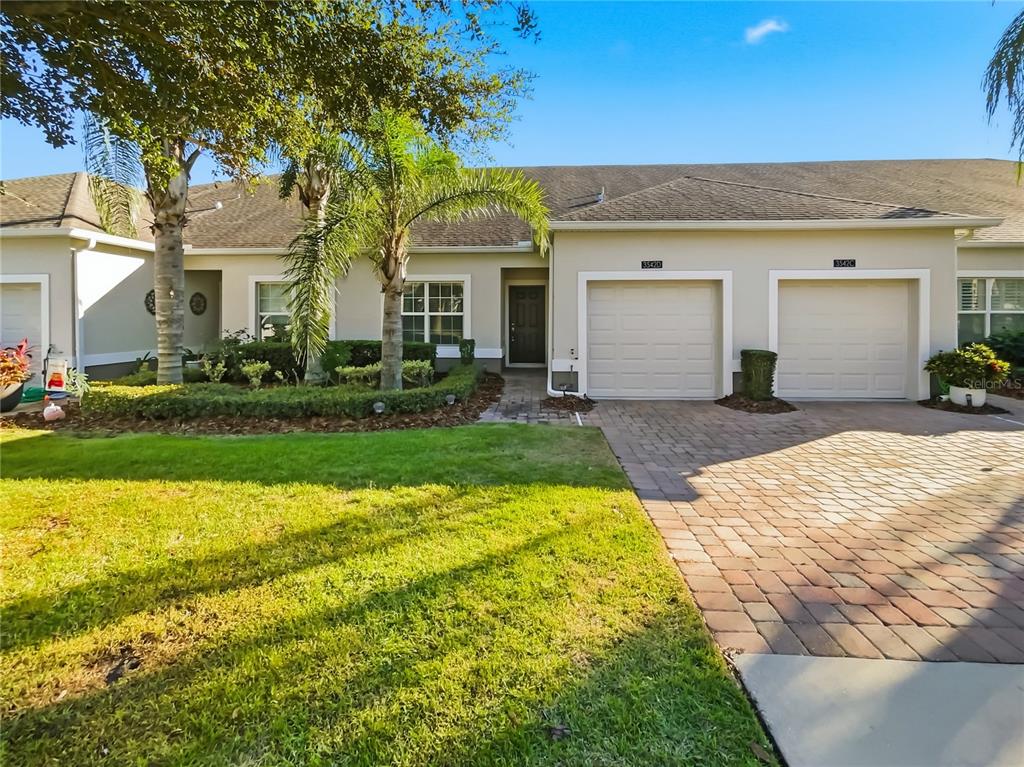 A single-story townhouse exterior features a paver driveway, two garage doors, and landscaped front yard — 3542 FAIRWATERS COURT UNIT D, CLERMONT, FL