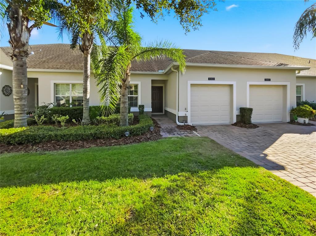 A single-story duplex with two garage doors, a paved driveway, and palm trees in front — 3542 FAIRWATERS COURT UNIT D, CLERMONT, FL