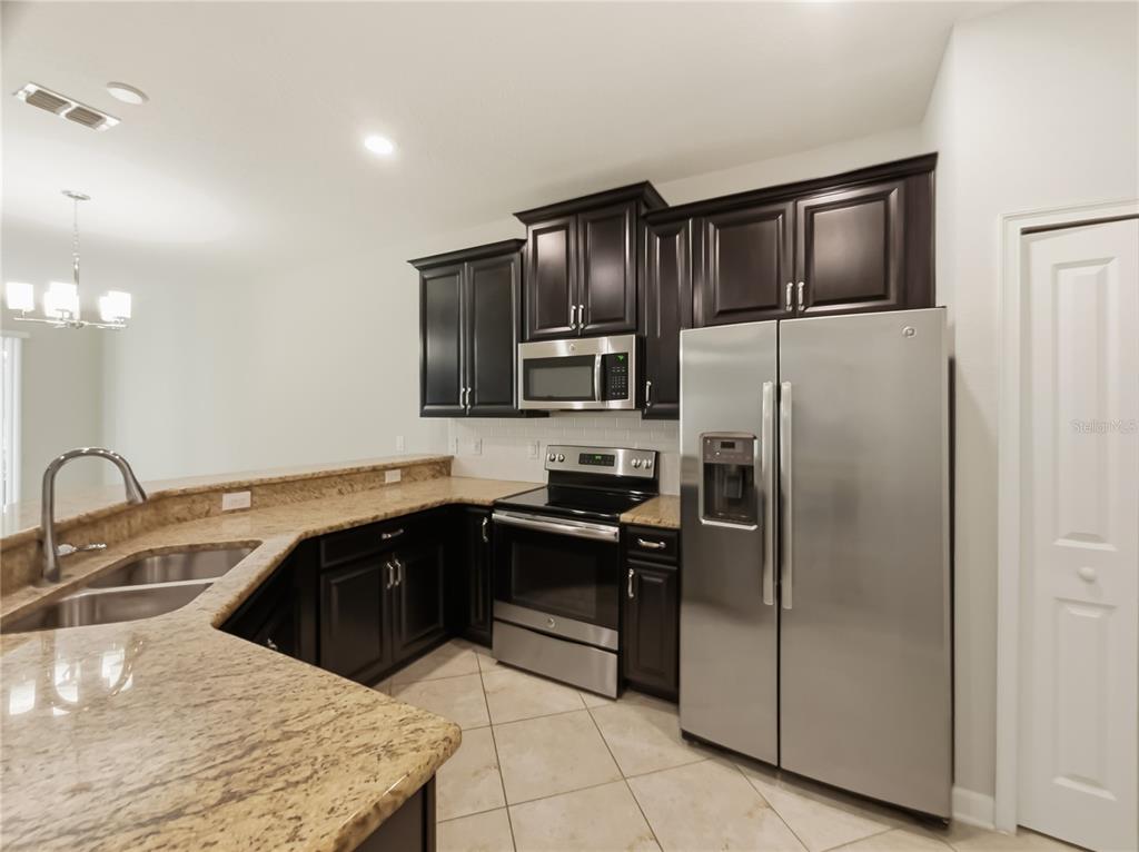 A kitchen features dark wood cabinets, granite countertops, stainless steel appliances, and tile flooring — 3542 FAIRWATERS COURT UNIT D, CLERMONT, FL