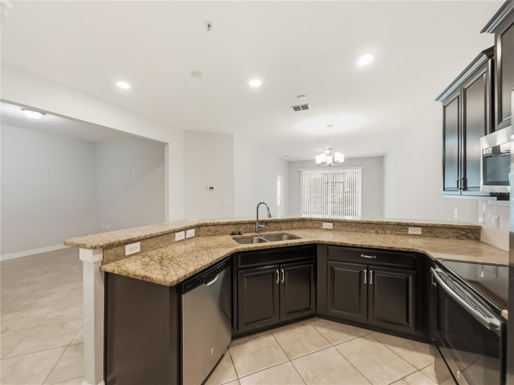 A kitchen with dark cabinets, granite countertops, and a stainless steel dishwasher — 3542 FAIRWATERS COURT UNIT D, CLERMONT, FL