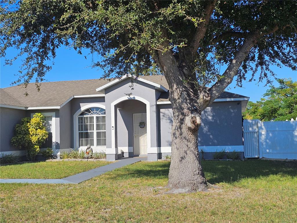 A gray single-story house with a white arched entryway and a large tree in front — 540 OAK BRANCH CIRCLE, KISSIMMEE, FL