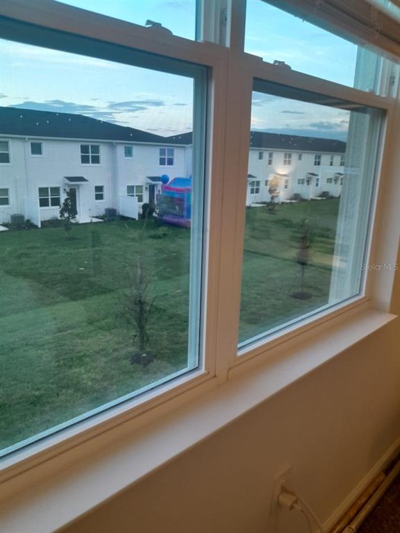 A view through a window shows a grassy backyard with townhomes and a bounce house — 113 BOGEY DRIVE, DAVENPORT, FL