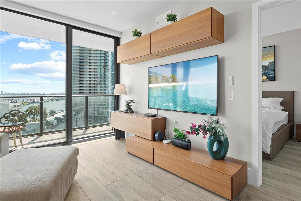 A modern living room features wood cabinetry, a wall-mounted television, and a balcony with city views — 501 NE 31st St # 1201, Miami FL 33137, MIAMI, FL