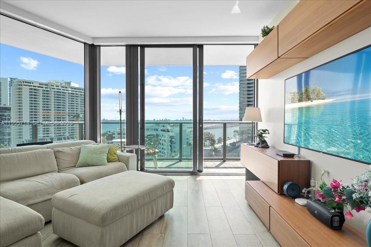 A living room features a light-colored sofa, a wall-mounted television, and a balcony overlooking water — 501 NE 31st St # 1201, Miami FL 33137, MIAMI, FL