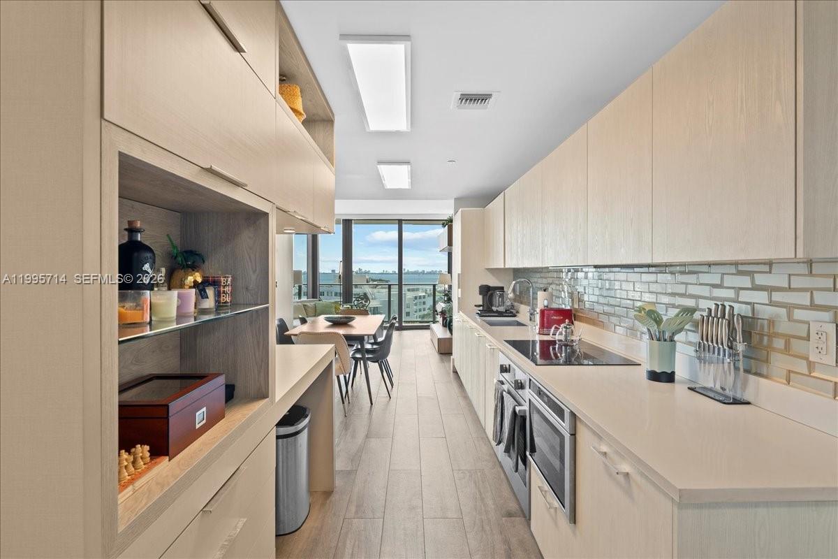 A modern galley kitchen features light wood cabinetry, quartz countertops, and a view of the ocean — 501 NE 31st St # 1201, Miami FL 33137, MIAMI, FL