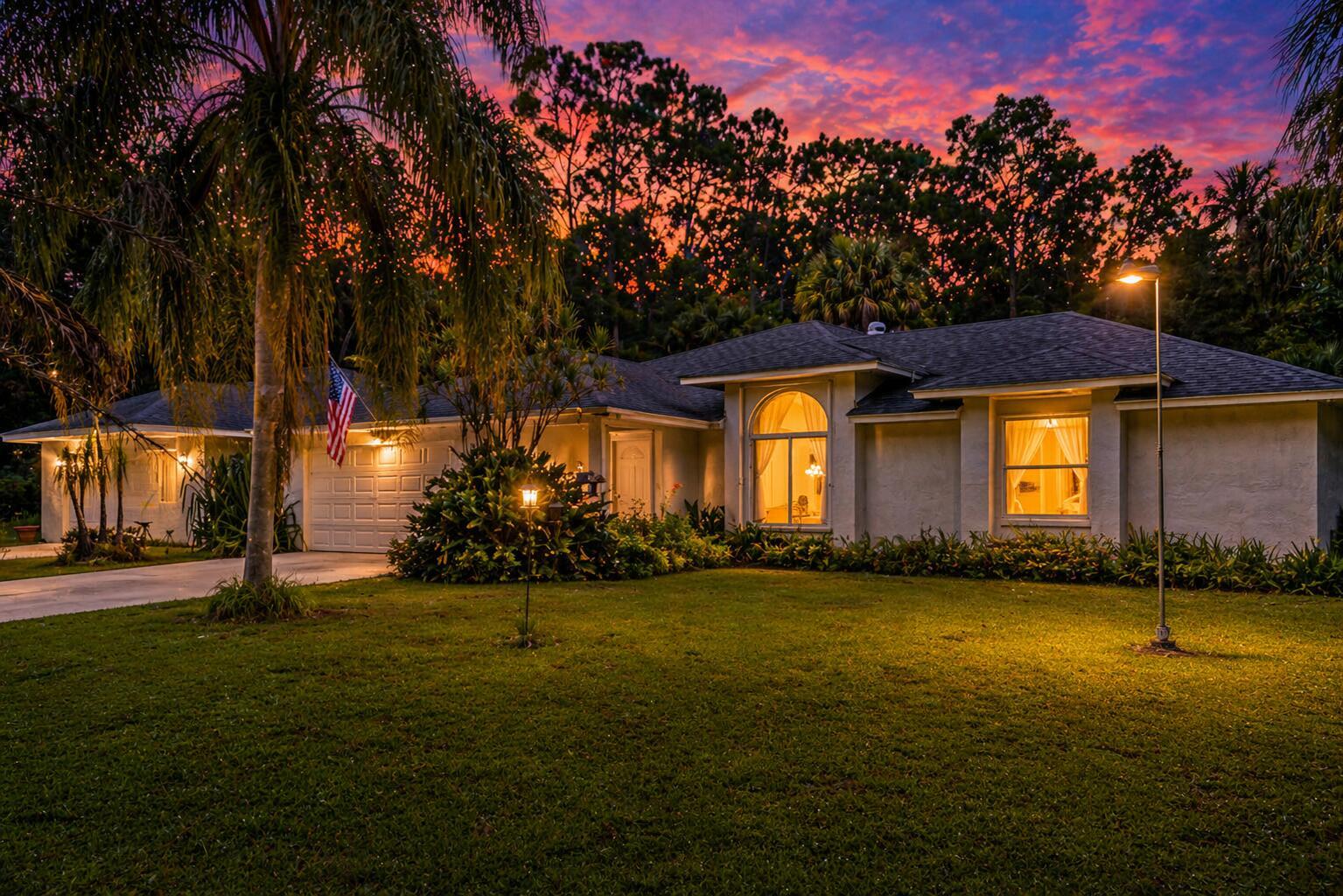 A single-story house with a white exterior, a garage, and a lawn at sunset — 15884 North Road, FL 33470, FL