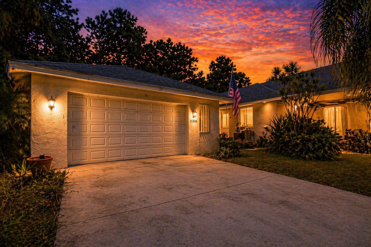 A single-story house with a two-car garage and an American flag at sunset — 15884 North Road, FL 33470, FL