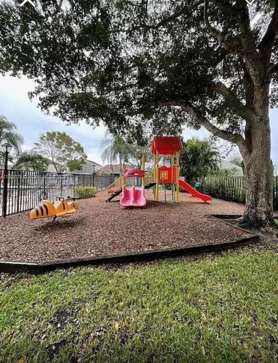 A playground with a slide structure and a bee-shaped spring rider under a large tree — 15813 W Waterside Circle # 206, Sunrise FL 33326, SUNRISE, FL