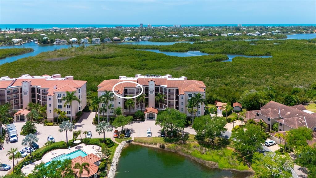 An aerial view shows a multi-story residential building with a circled balcony overlooking a pond — 5420 EAGLES POINT CIRCLE UNIT 402, SARASOTA, FL