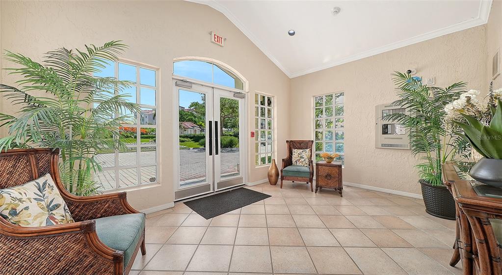 A bright lobby features tile floors, wicker furniture, potted plants, and double glass entry doors — 5420 EAGLES POINT CIRCLE UNIT 402, SARASOTA, FL