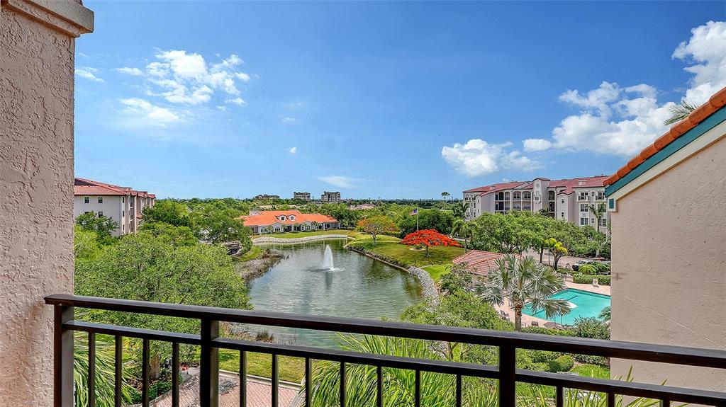 A balcony view overlooking a pond with a fountain, lush landscaping, and surrounding apartment buildings — 5420 EAGLES POINT CIRCLE UNIT 402, SARASOTA, FL