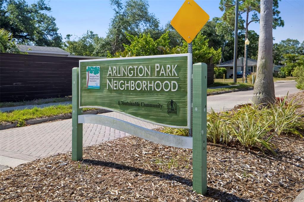 A green and white neighborhood sign stands in a mulched garden bed near a road — 2114 FLOYD STREET, SARASOTA, FL