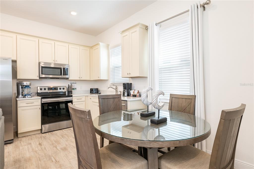 A kitchen with cream cabinets, stainless steel appliances, and a glass-topped dining table — 2956 SALTED RIM ROAD, KISSIMMEE, FL