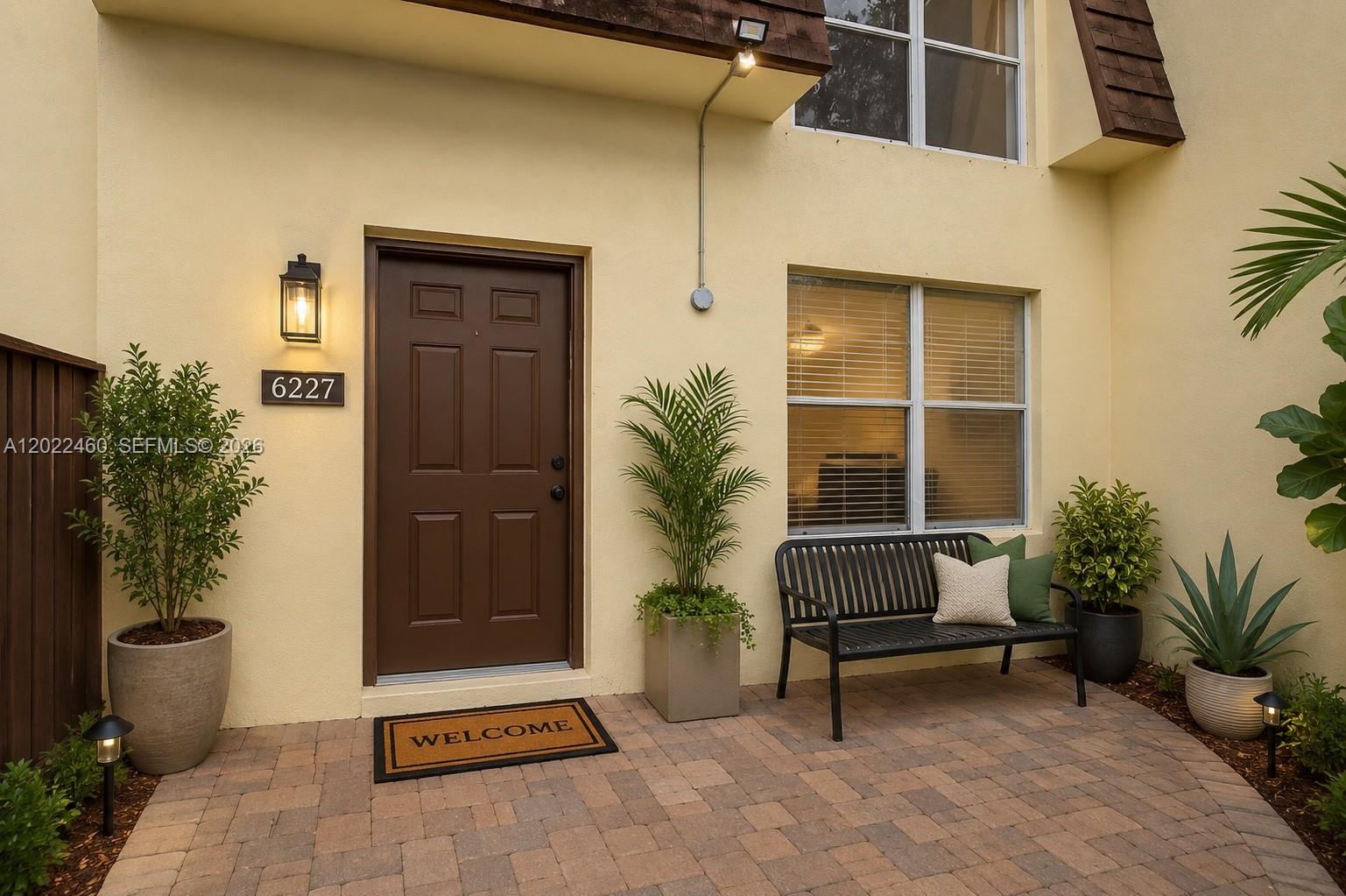 A paved patio entrance features a brown door, a black bench, and several potted plants — 3764 SW 60th Ter # 15, Davie FL 33314, DAVIE, FL