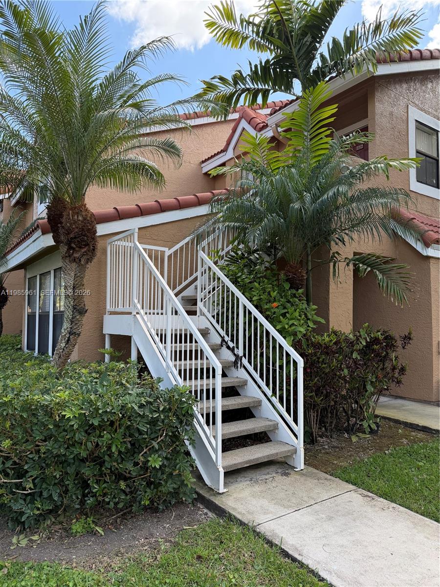 An exterior view of a two-story tan building with a white metal staircase and palms — 10500 SW 155th Ct # 1026, Miami FL 33196, MIAMI, FL