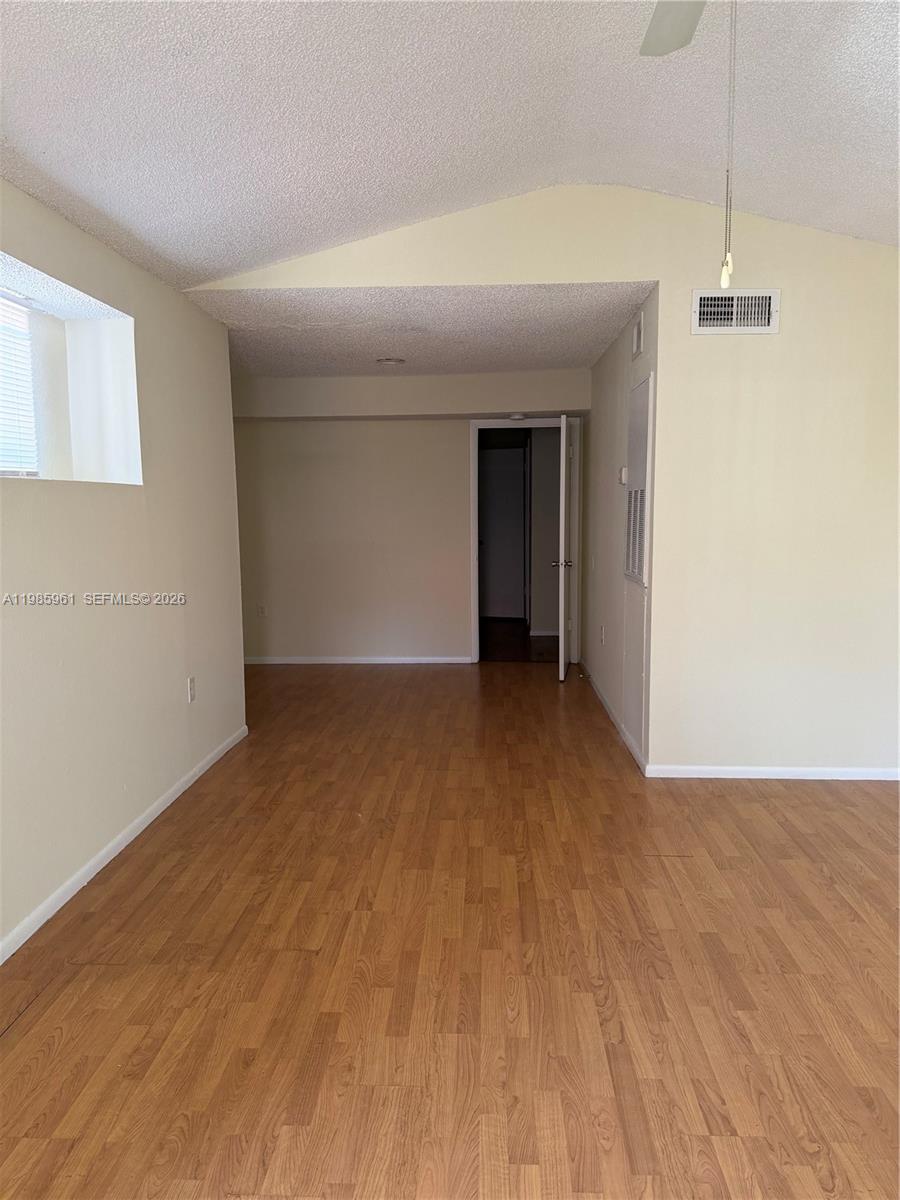 An empty room features light wood-look flooring, beige walls, and a vaulted ceiling — 10500 SW 155th Ct # 1026, Miami FL 33196, MIAMI, FL