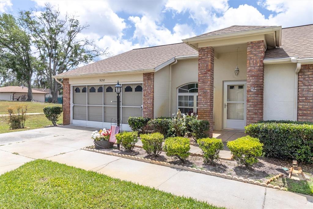 A single-story house features a brick-accented entryway, a two-car garage, and a landscaped front yard — 9058 ARUNDLE PLACE, NEW PORT RICHEY, FL