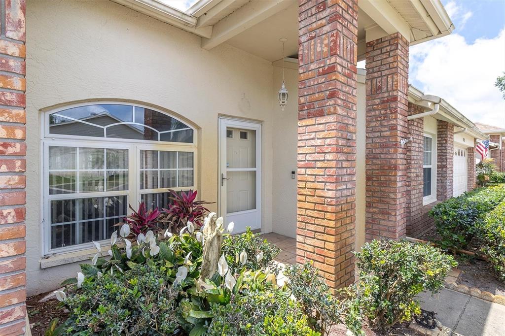 The exterior of a house features a brick-columned entryway, a large arched window, and landscaping — 9058 ARUNDLE PLACE, NEW PORT RICHEY, FL