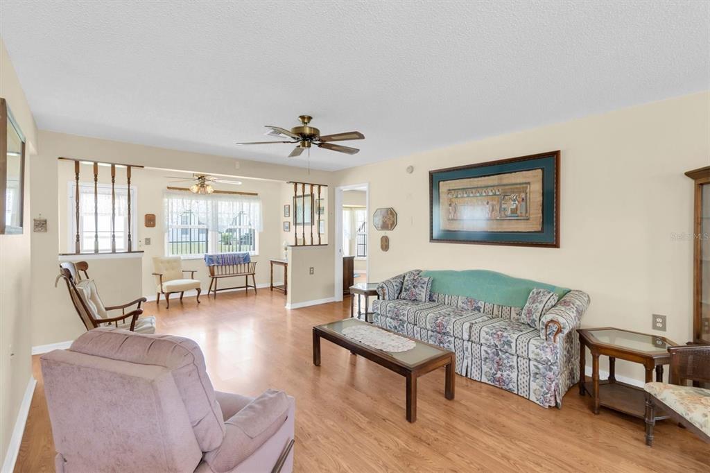 A living room with wood-look flooring, a floral sofa, and a ceiling fan — 9058 ARUNDLE PLACE, NEW PORT RICHEY, FL
