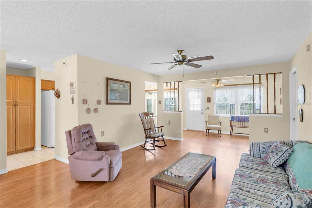 A living room with light-colored walls, wood-look flooring, a ceiling fan, and floral furniture — 9058 ARUNDLE PLACE, NEW PORT RICHEY, FL