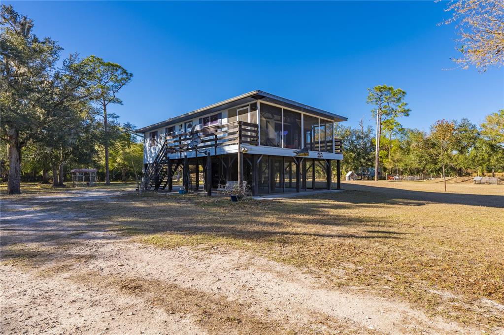 An elevated house with a screened porch and wooden deck stands on a grassy lot — 2207 SW BLOSSOM AVENUE, ARCADIA, FL