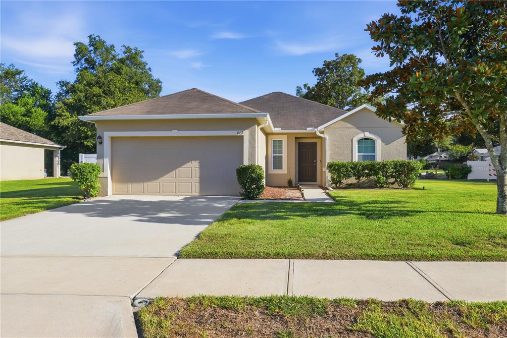 A single-story house with a beige stucco exterior, a two-car garage, and a front lawn — 802 GRAND PARK COURT, DELAND, FL