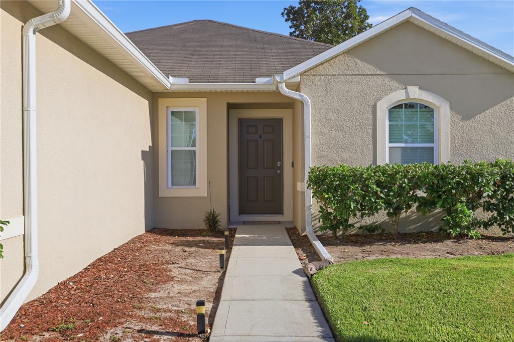 The exterior of a beige stucco house features a brown front door and concrete walkway — 802 GRAND PARK COURT, DELAND, FL
