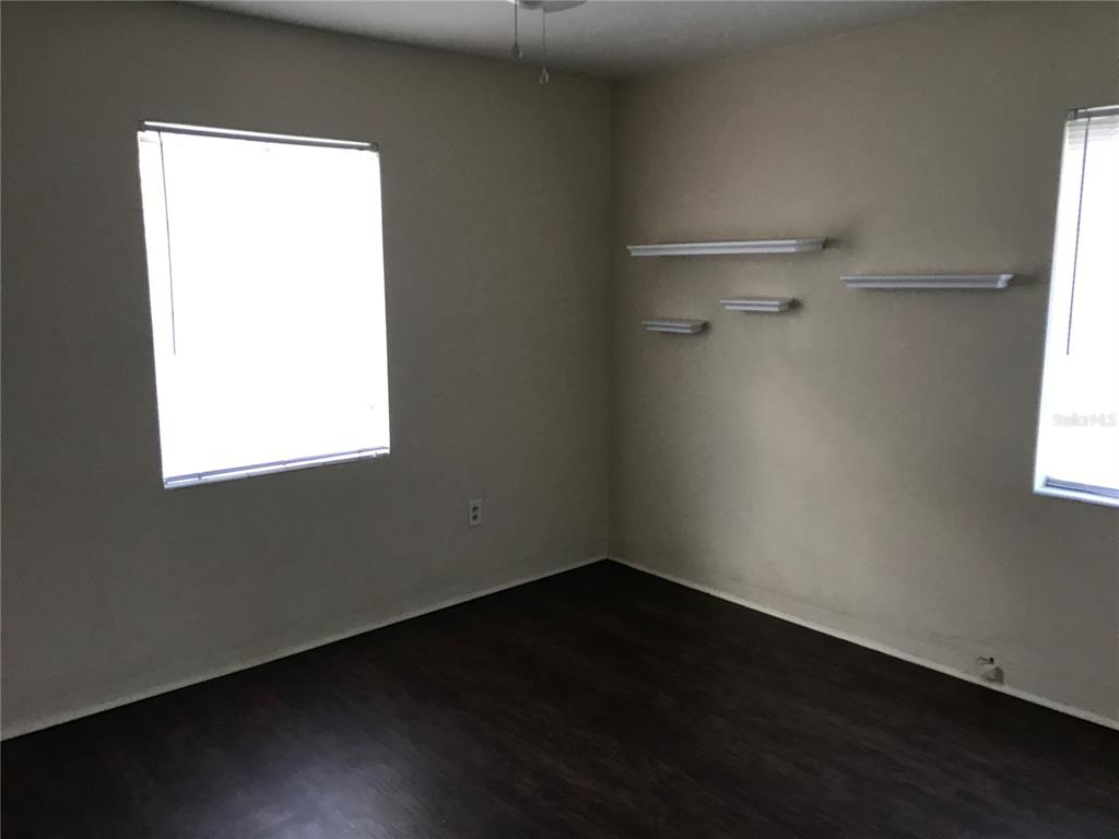 An empty bedroom features dark wood-look flooring, beige walls, two windows, and four wall-mounted shelves — 118 RIGGINS STREET, LAKELAND, FL