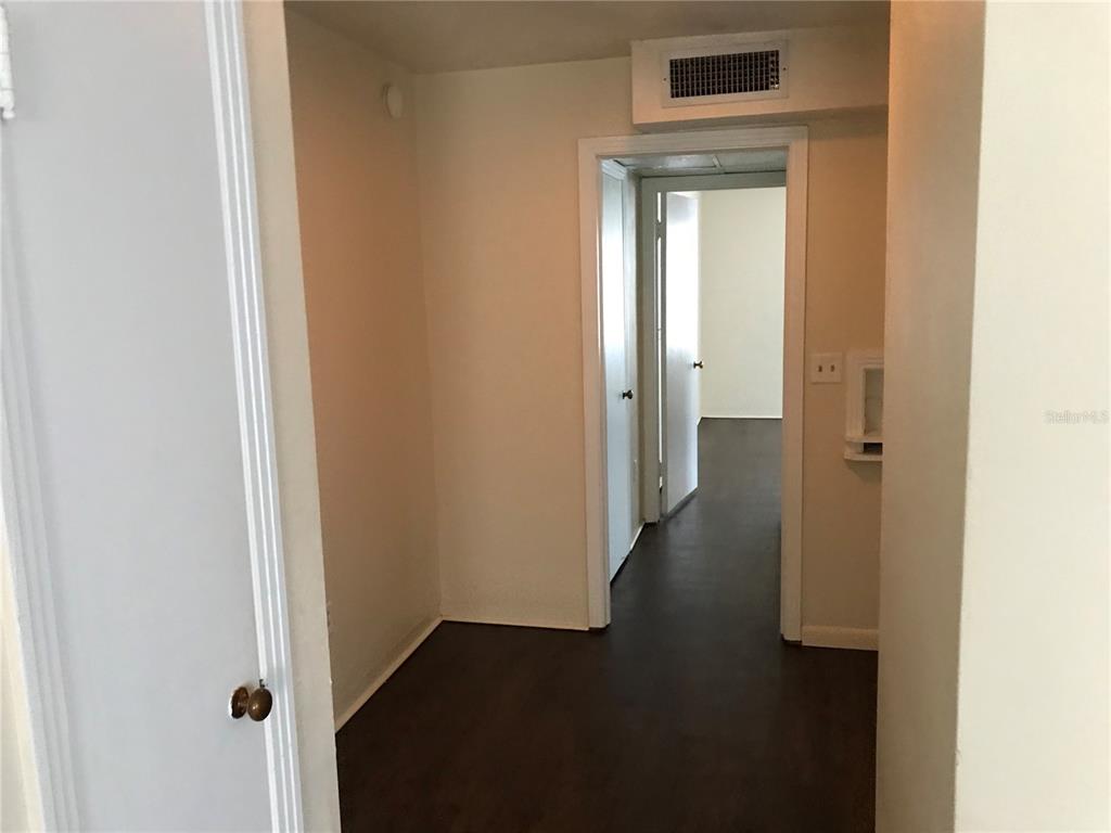 A hallway with dark wood-look flooring leads to a doorway and an adjacent room — 118 RIGGINS STREET, LAKELAND, FL