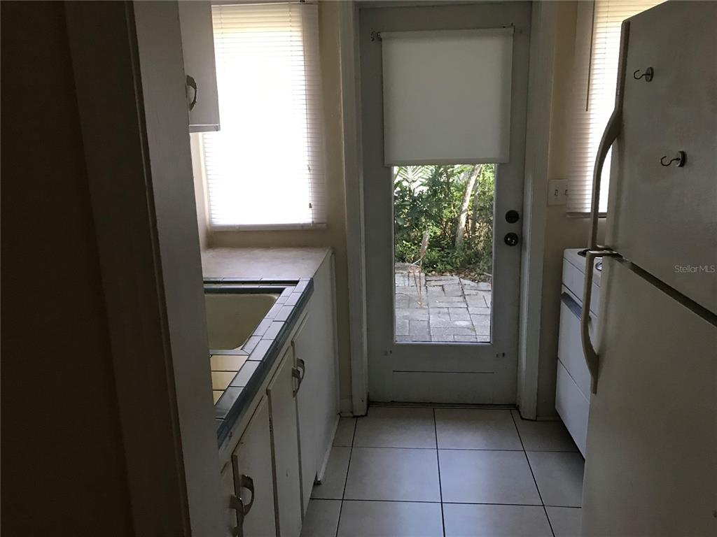 A small kitchen features white cabinets, tiled countertops, a refrigerator, and a glass-paneled exterior door — 118 RIGGINS STREET, LAKELAND, FL
