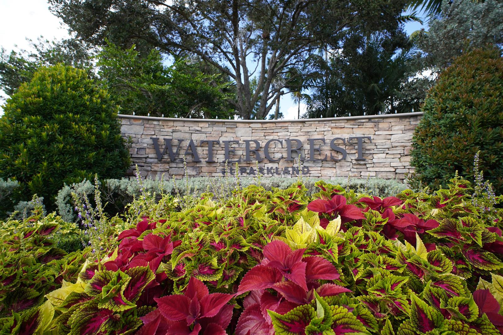 A stone sign for Watercrest at Parkland stands behind a bed of colorful coleus plants — 8965 Watercrest Circle E, Parkland FL 33076, PARKLAND, FL