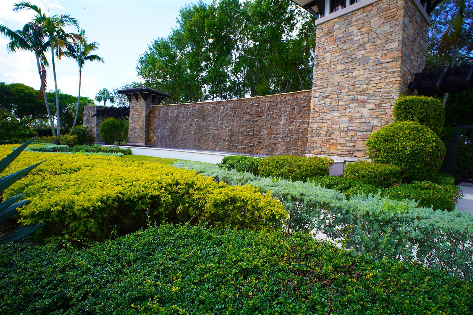 A stone water feature wall stands behind manicured landscaping and palm trees — 8965 Watercrest Circle E, Parkland FL 33076, PARKLAND, FL