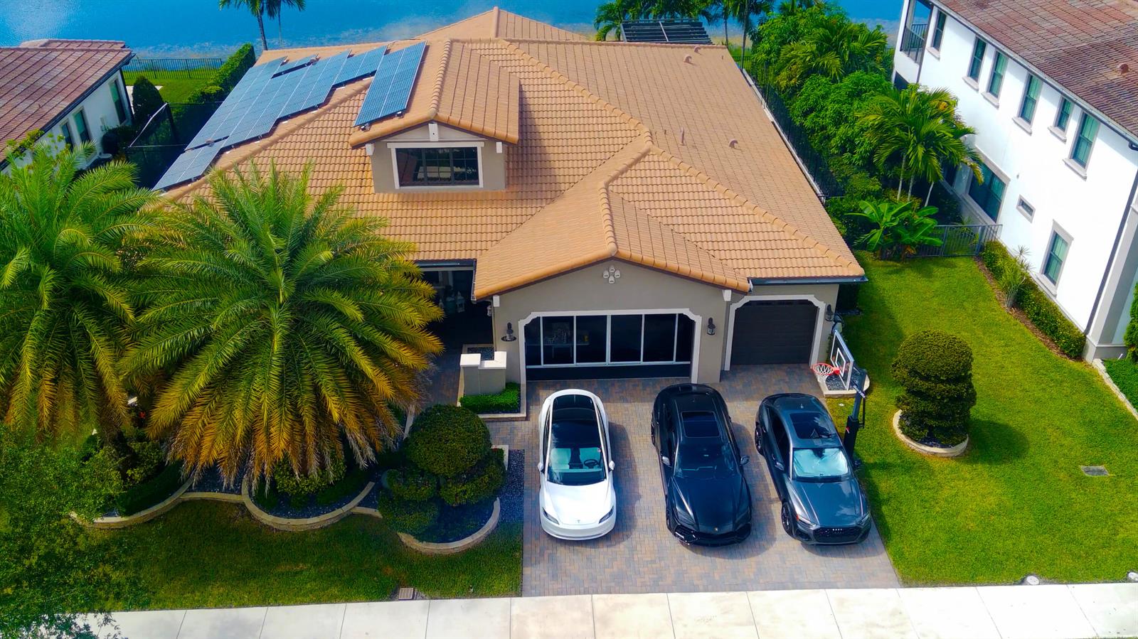 An aerial view of a suburban house with solar panels, three parked cars, and landscaping — 8965 Watercrest Circle E, Parkland FL 33076, PARKLAND, FL