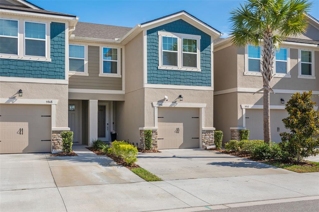 A row of three two-story townhomes with beige stucco, blue shingle accents, and attached garages — 5950 GRAND SONATA AVENUE, LUTZ, FL