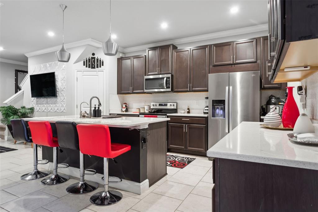 A kitchen features dark wood cabinets, a white quartz island, and red bar stools — 5950 GRAND SONATA AVENUE, LUTZ, FL