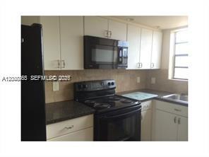 A kitchen features white cabinets, black appliances, a dark countertop, and a tiled backsplash — 7740 Abbott Ave # 5B, Miami Beach FL 33141, MIAMI BEACH, FL