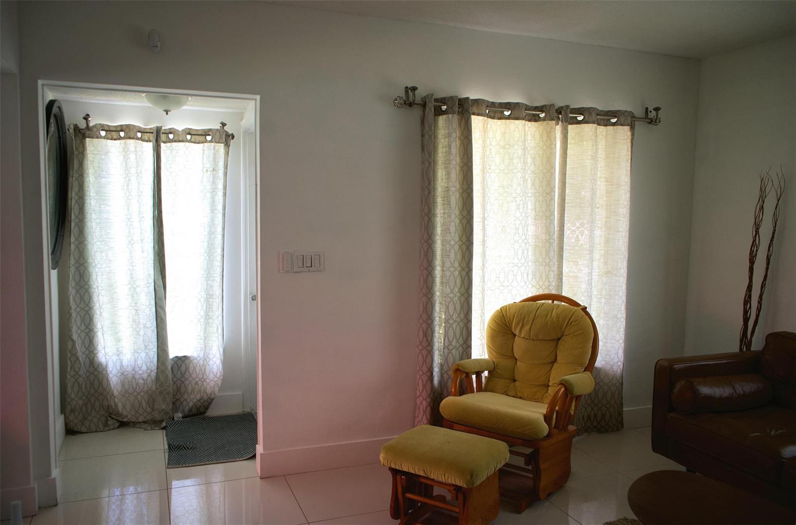 A living room features a yellow rocking chair, a matching ottoman, and floor-to-ceiling curtains — 11150 Peachtree Drive, Miami FL 33161, MIAMI, FL