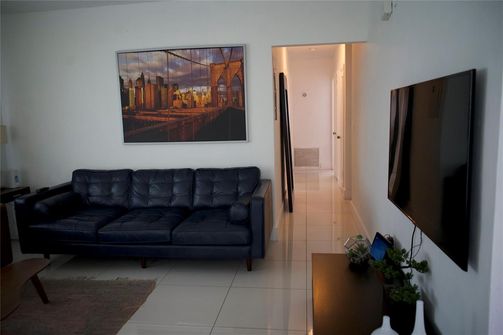 A living room features a dark leather sofa, a wall-mounted television, and tile flooring — 11150 Peachtree Drive, Miami FL 33161, MIAMI, FL