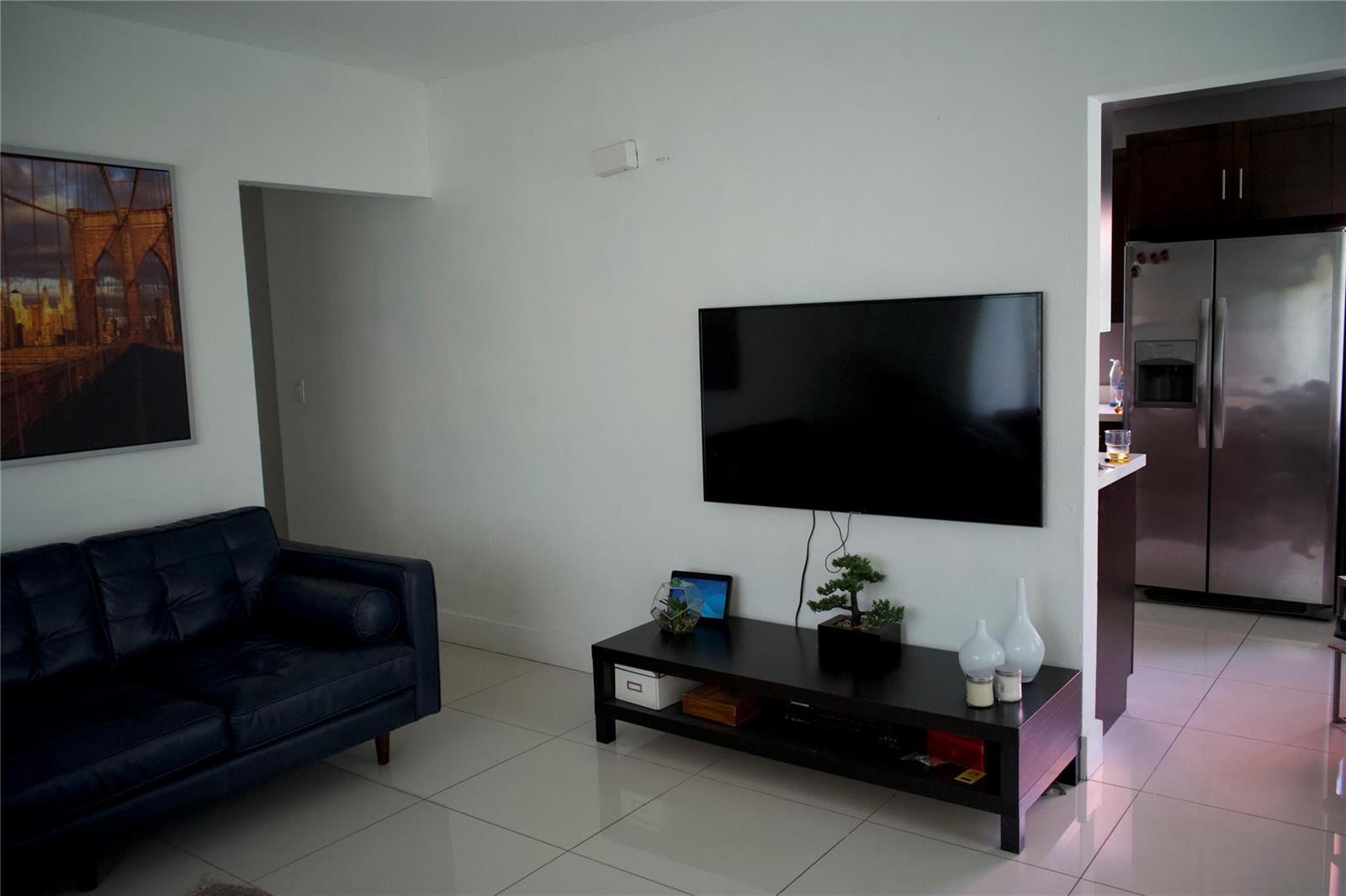 A living room features a dark leather sofa, a wall-mounted television, and a media console — 11150 Peachtree Drive, Miami FL 33161, MIAMI, FL