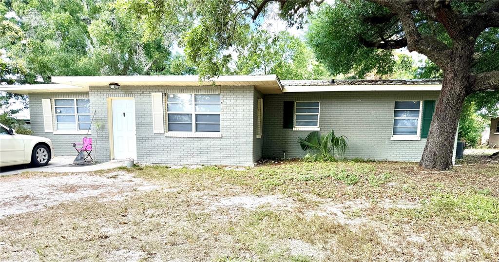 A single-story gray brick house with a white door and a large tree in front — 1405 AVENUE H SW, WINTER HAVEN, FL